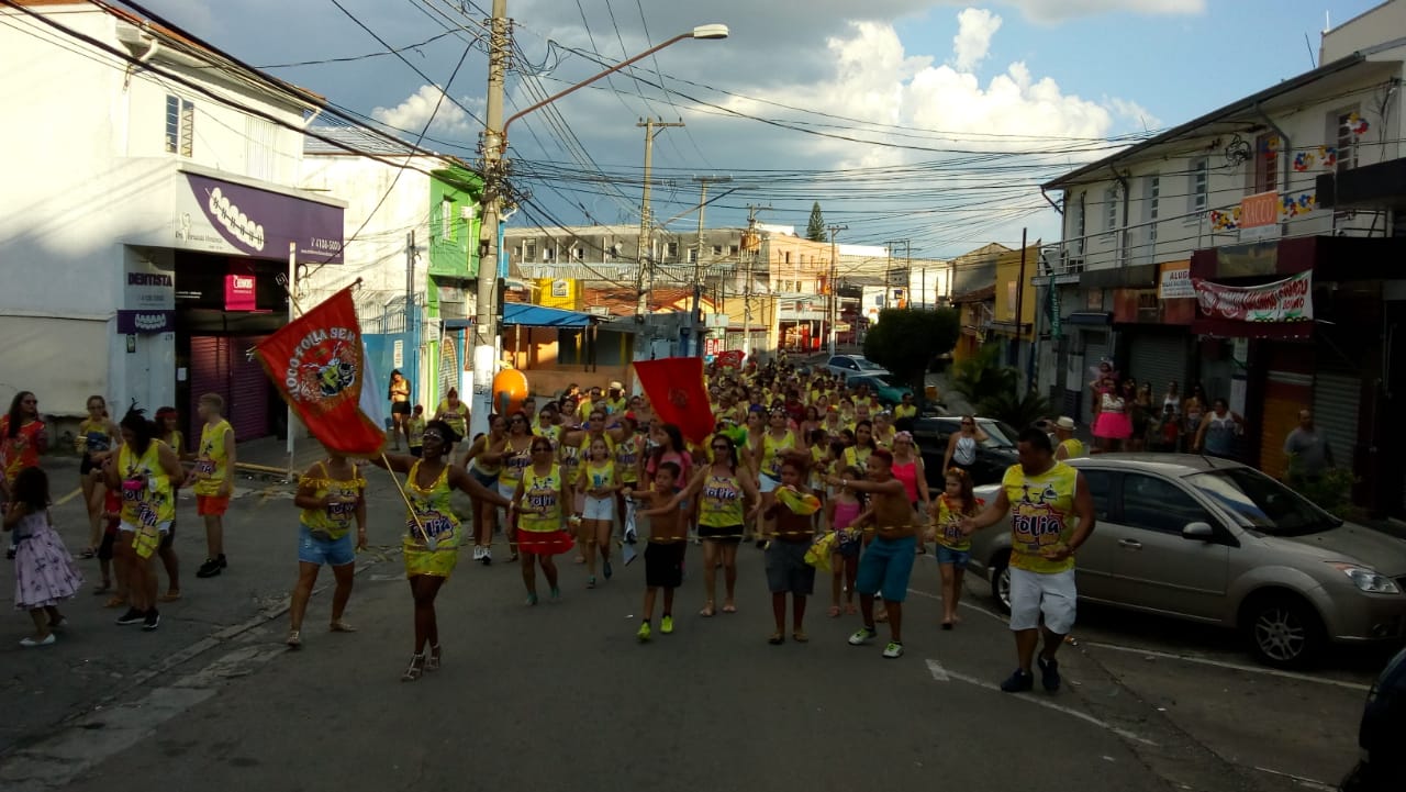 Cerca de trinta pessoas vestidas com abadá na cor amarela, desfilando no meio da rua
